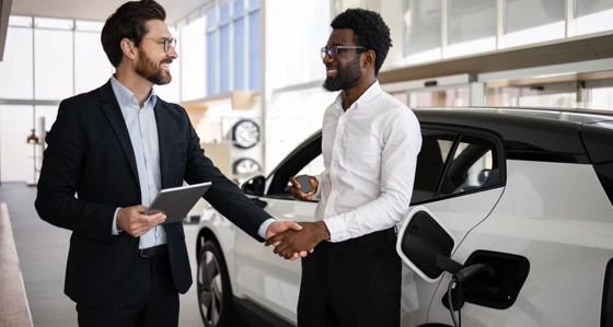 A car dealer and a customer shaking hands at a car dealership