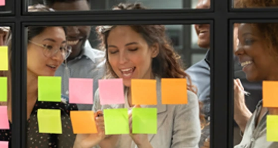 Four people looking at post its on a glass interior window